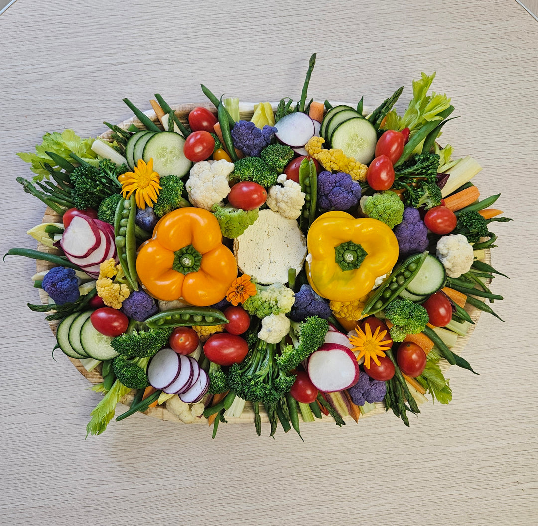 A platter of fresh vegetables including cucumbers, tomatoes, bell peppers, radishes, and lettuce, arranged in an attractive pattern, accompanied by  two dips.