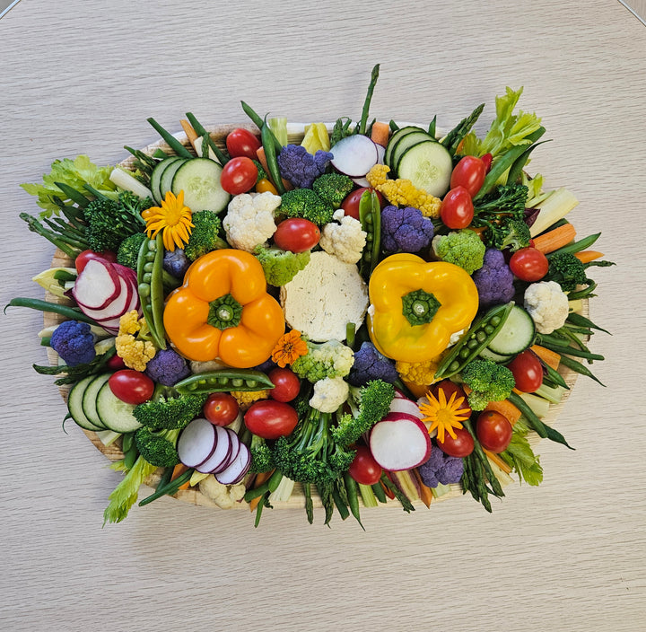 A platter of fresh vegetables including cucumbers, tomatoes, bell peppers, radishes, and lettuce, arranged in an attractive pattern, accompanied by  two dips.