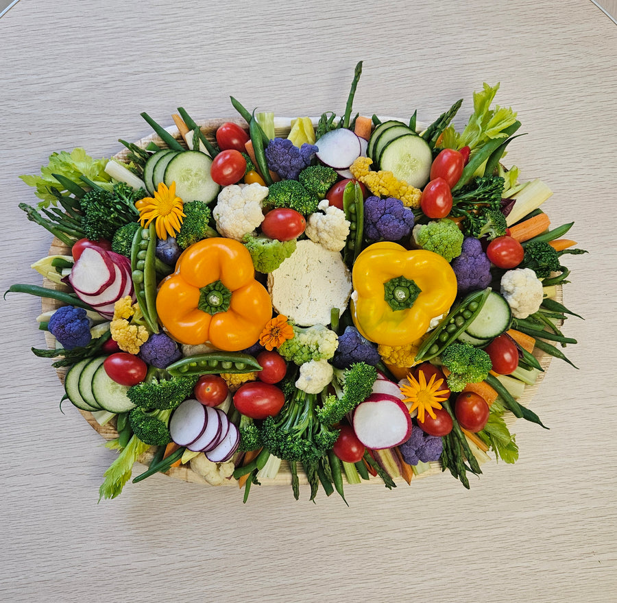A platter of fresh vegetables including cucumbers, tomatoes, bell peppers, radishes, and lettuce, arranged in an attractive pattern, accompanied by  two dips.